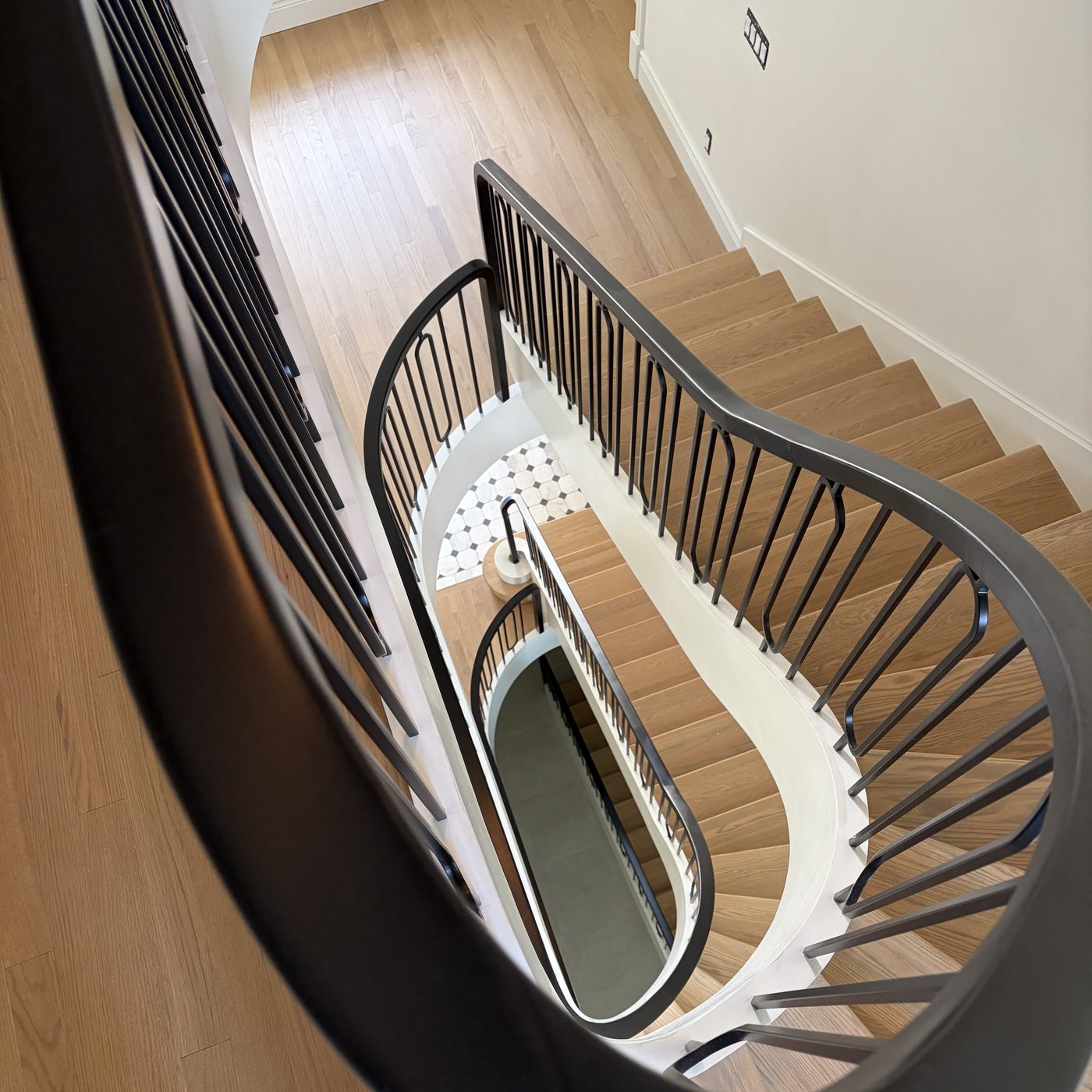 Vue en plongée d'un escalier courbe : volute complète, limon cintré et rampe en fer forgé noir